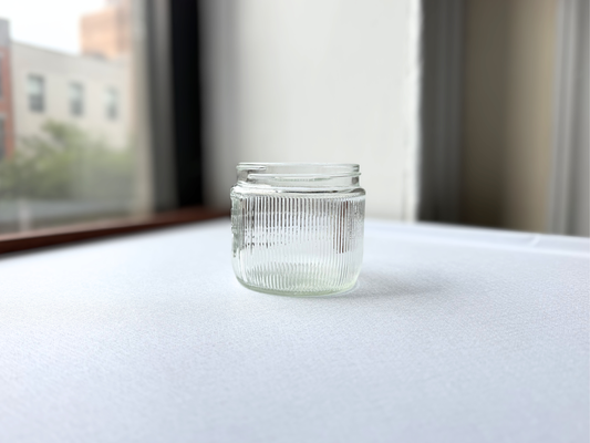 Vintage clear glass Burma-Shave jar with ribbed texture, shown at a three-quarter angle highlighting its Burma-Vita Company branding and textured surface.