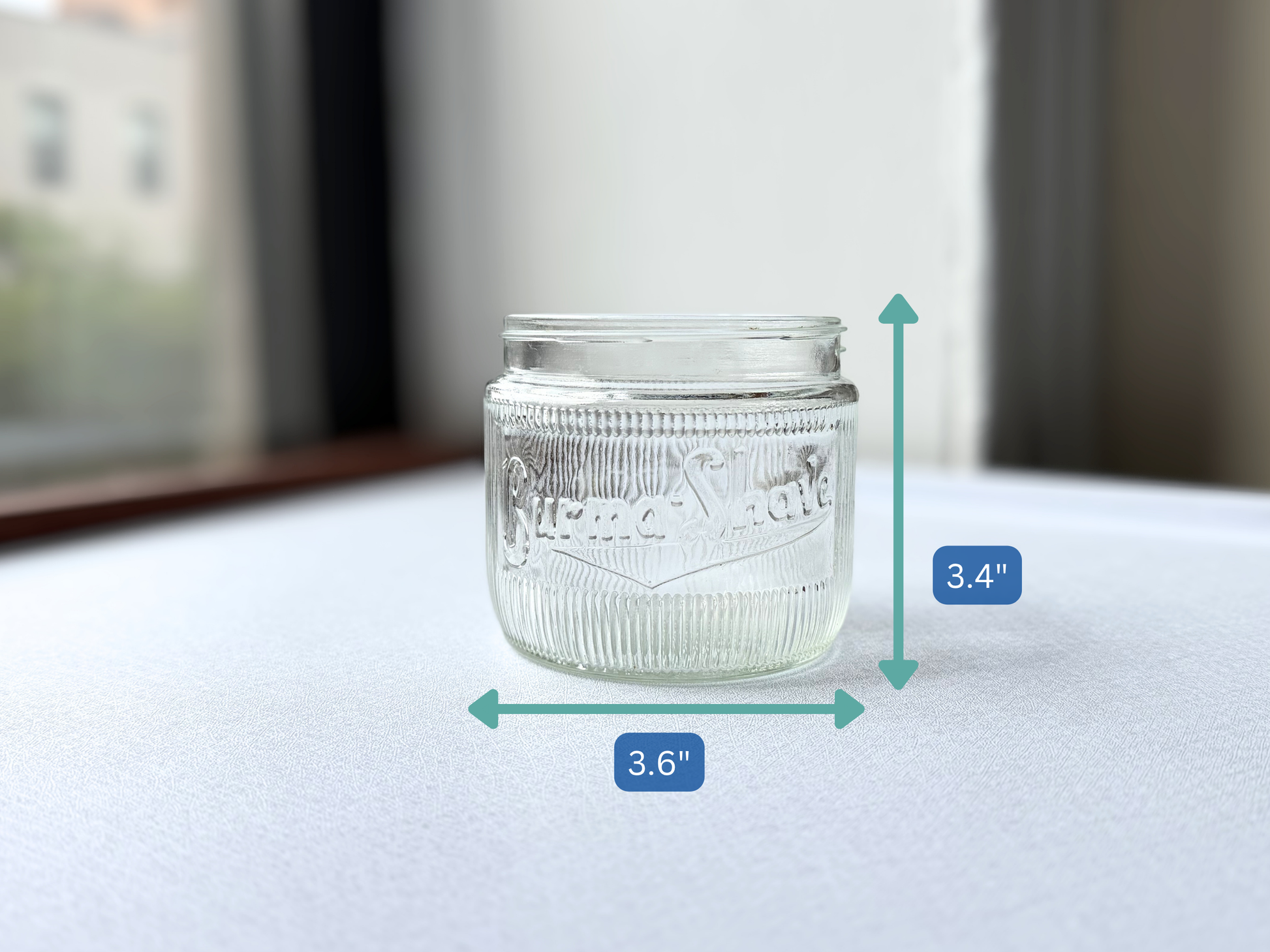 Vintage ribbed glass Burma-Shave jar shown with measurement markers indicating a height of 3.4 inches and width of 3.6 inches, illustrating its compact, squat scale.
