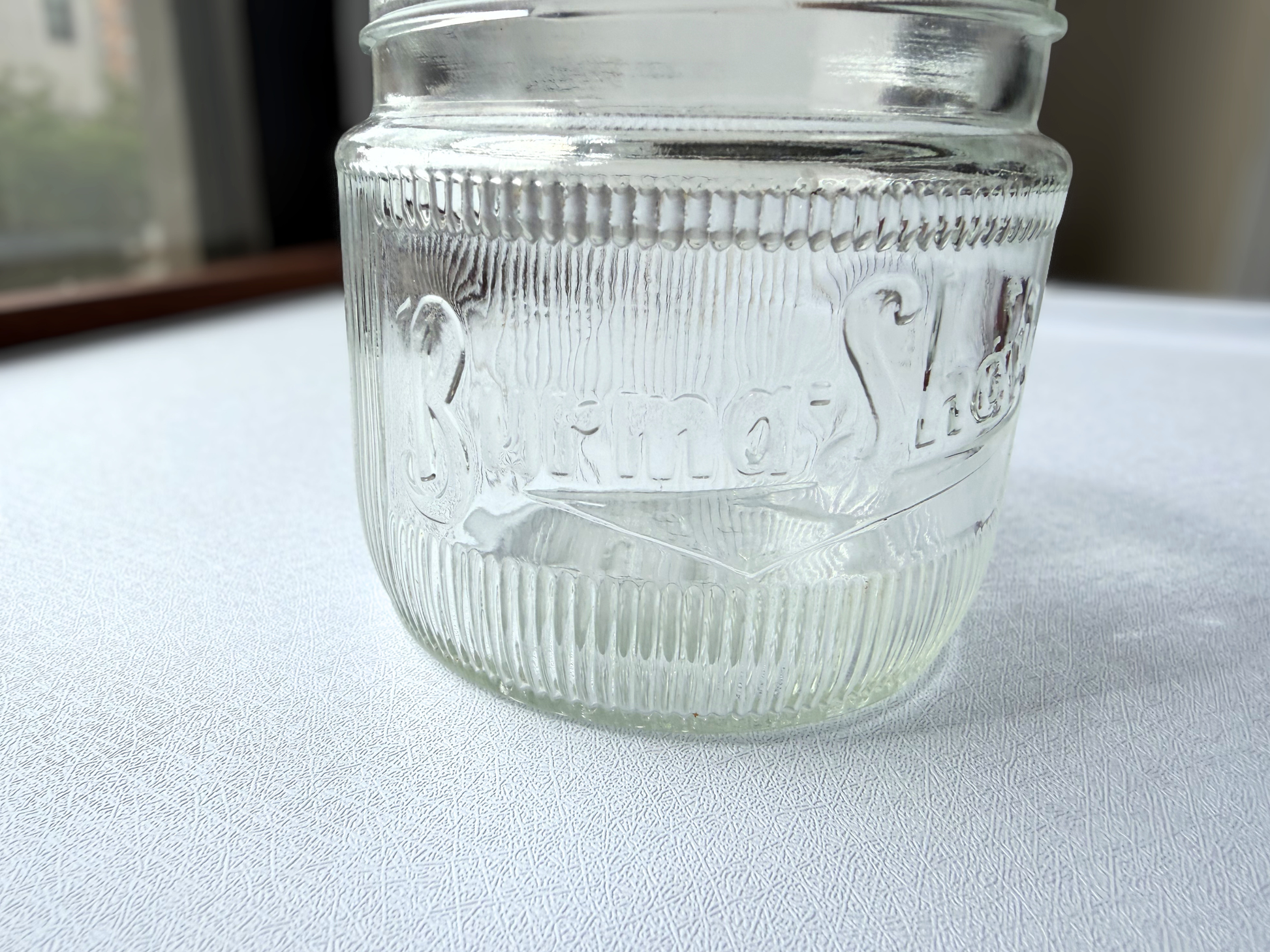 Close-up of the Burma-Shave logo embossed on the front of a vintage ribbed glass jar, showing crisp lettering despite decades of age.