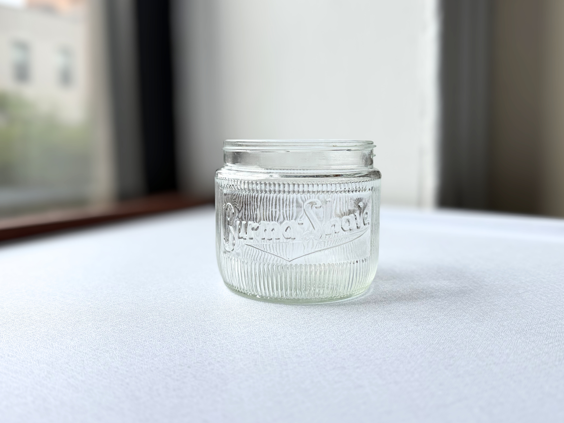 Front view of a vintage clear glass Burma-Shave jar with ribbed texture and embossed logo, ideal for a vintage apothecary or bathroom shelf display.