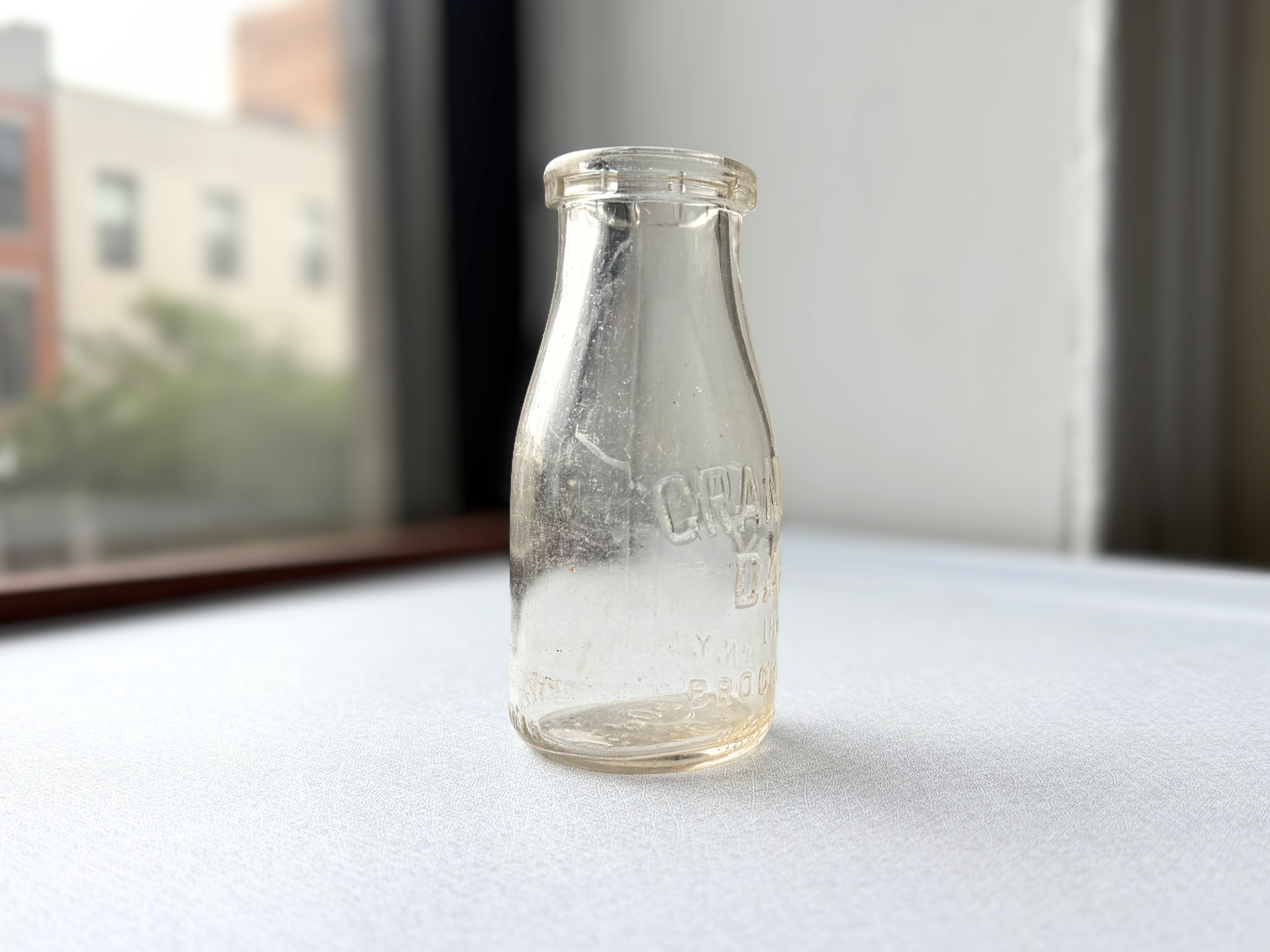 Vintage clear glass Grandview Dairy half-pint milk bottle from Brooklyn, NY, shown at a three-quarter angle highlighting its compact, tidy mid-century dairy bottle shape.
