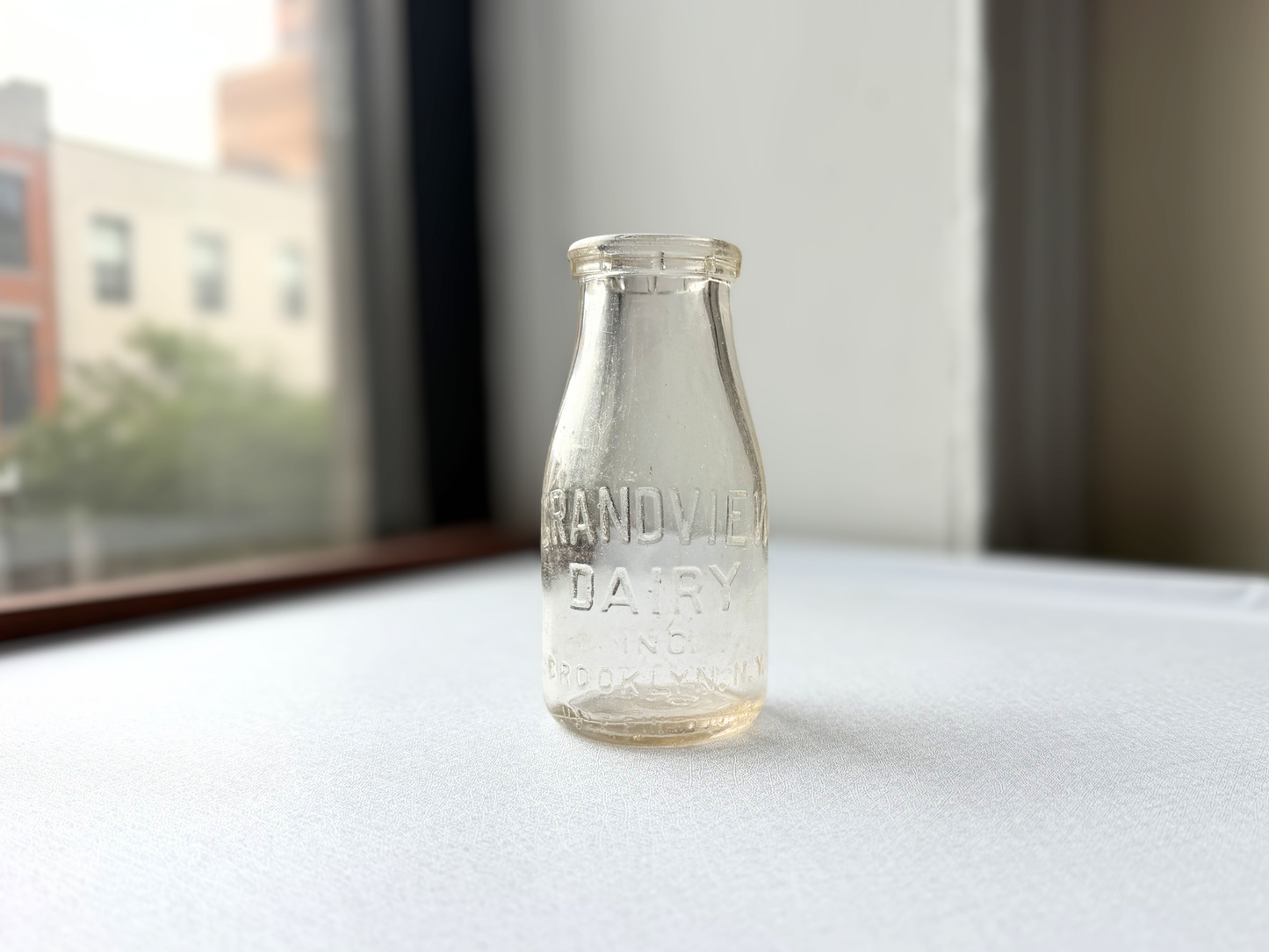 Front view of a vintage clear glass Grandview Dairy Inc. Brooklyn NY half pint milk bottle, showing its compact silhouette and legible embossed lettering.