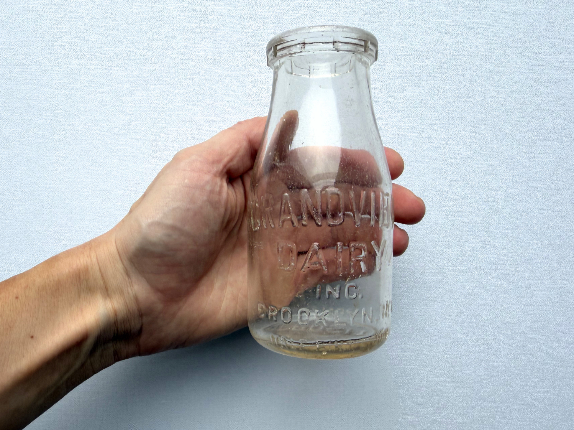 A hand holding a vintage Grandview Dairy milk bottle, providing a scale reference showing its small, tidy 5.25-inch height ideal for a kitchen windowsill bud vase.