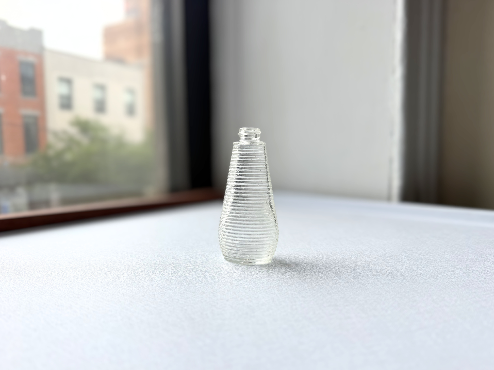 Small vintage clear glass ribbed bottle with a rounded halo shoulder, once used for shampoo, shown at a three-quarter angle highlighting its textured surface.
