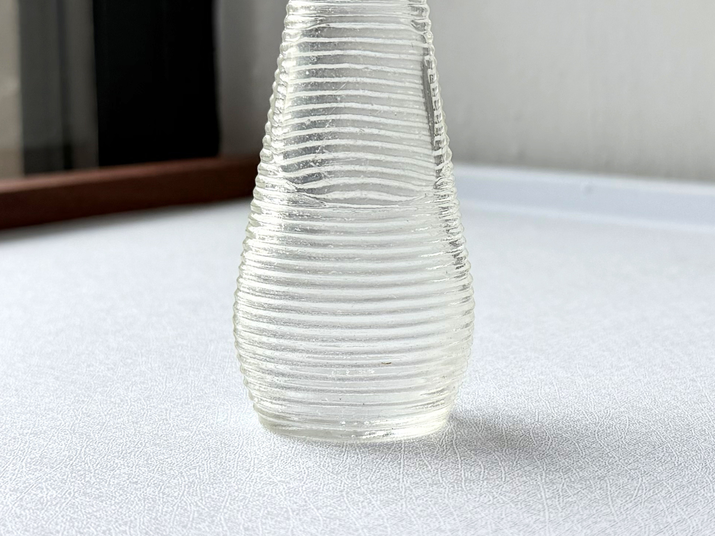 Close-up of the ribbed texture on a small vintage clear glass halo shampoo bottle, showing the distinctive vertical grooves that catch and scatter light.