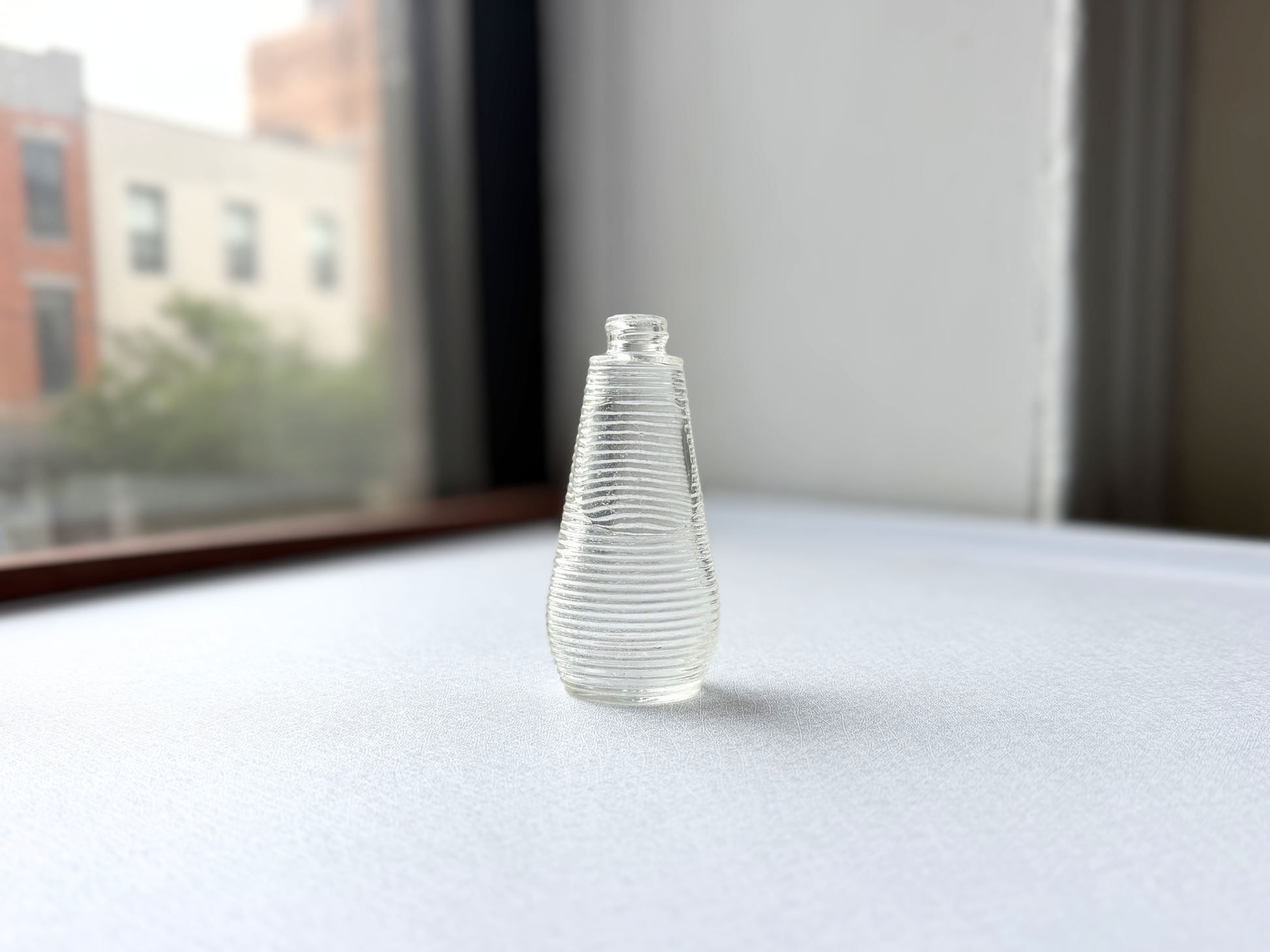 Front view of a small vintage clear glass bottle with ribbed texture and a rounded halo shoulder, ideal for a ring dish or miniature bud vase.
