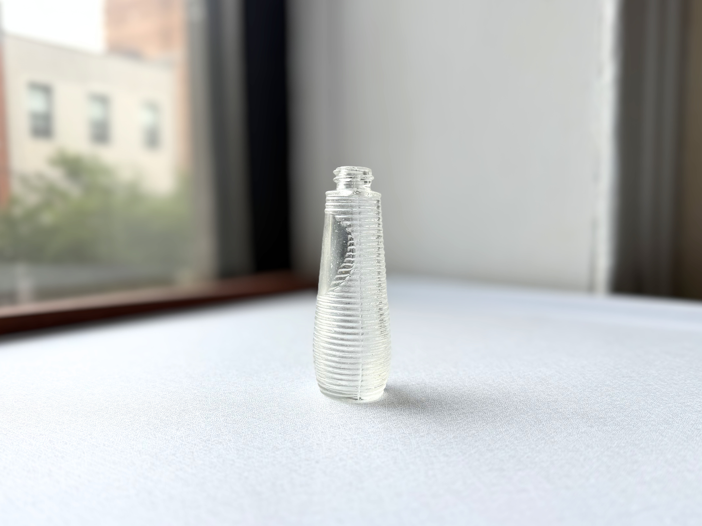 Full length view of a small vintage ribbed glass halo bottle standing upright, showing its compact, textured silhouette.