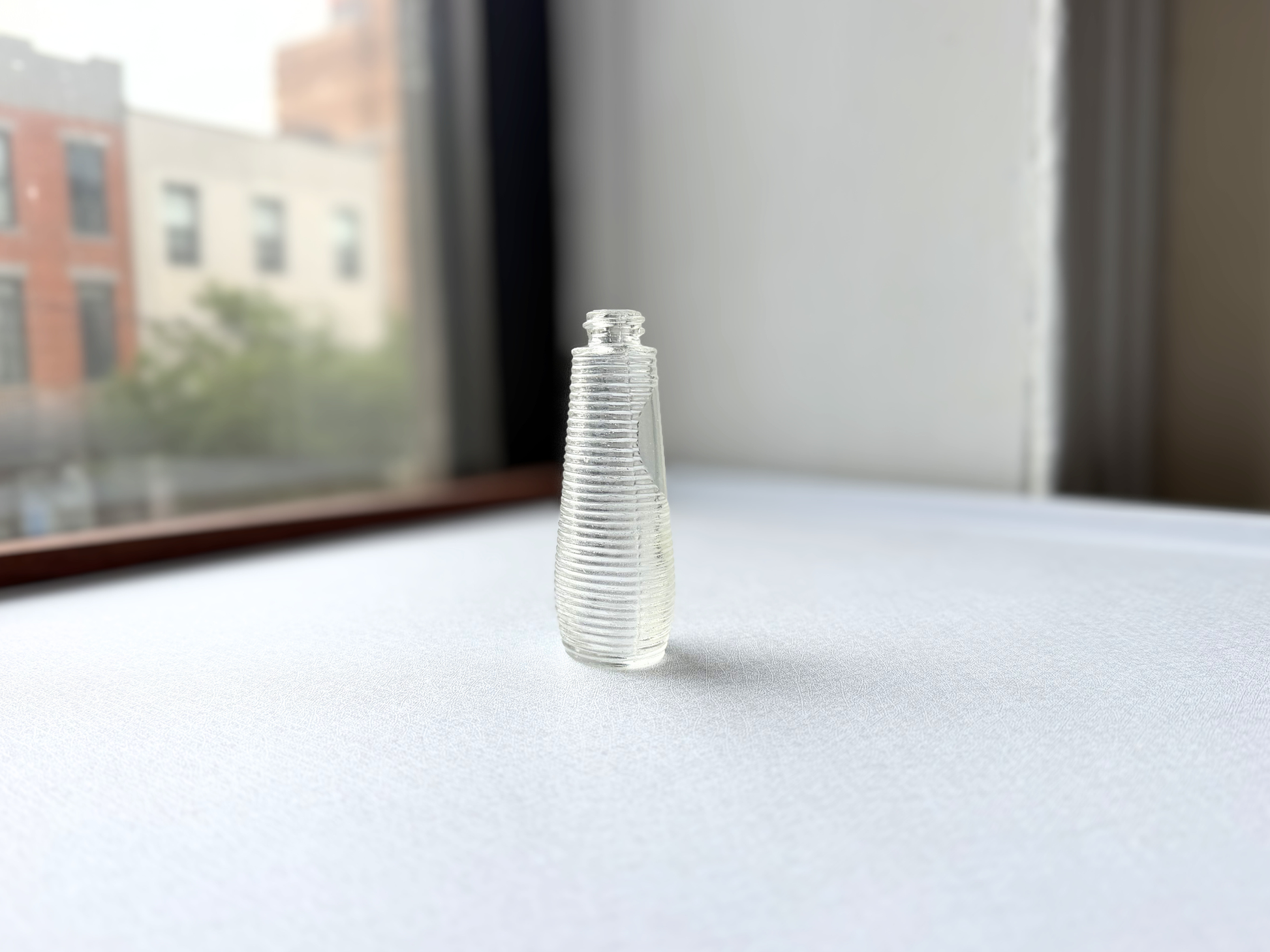 Side view of a small vintage ribbed glass halo bottle showing its rounded halo shoulder and textured body, suited for a grouped vanity shelf display.