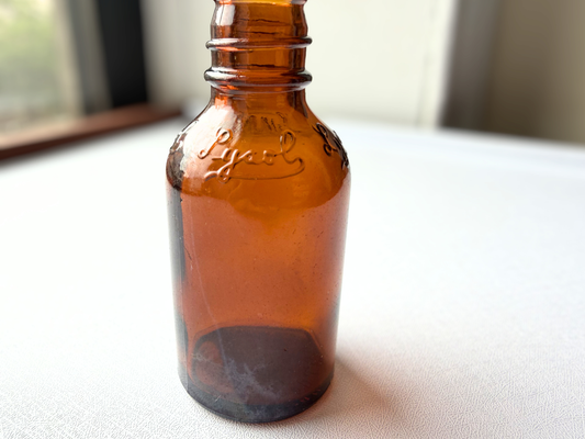 Close-up of the Lysol logo embossed on the front of a vintage amber glass apothecary bottle, showing crisp lettering despite decades of age.