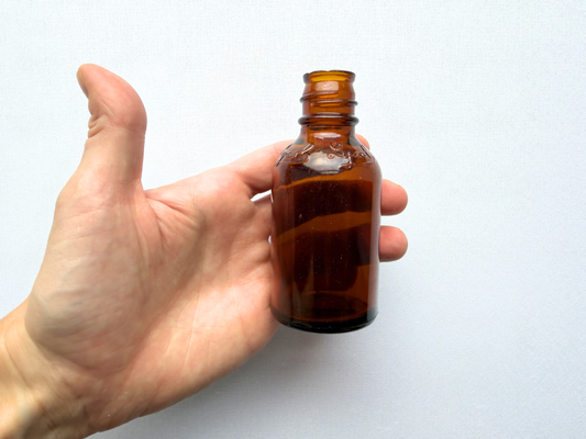 A hand holding a small vintage amber glass Lysol bottle, providing a scale reference that shows its compact 4-inch height ideal for a medicine cabinet shelf display.