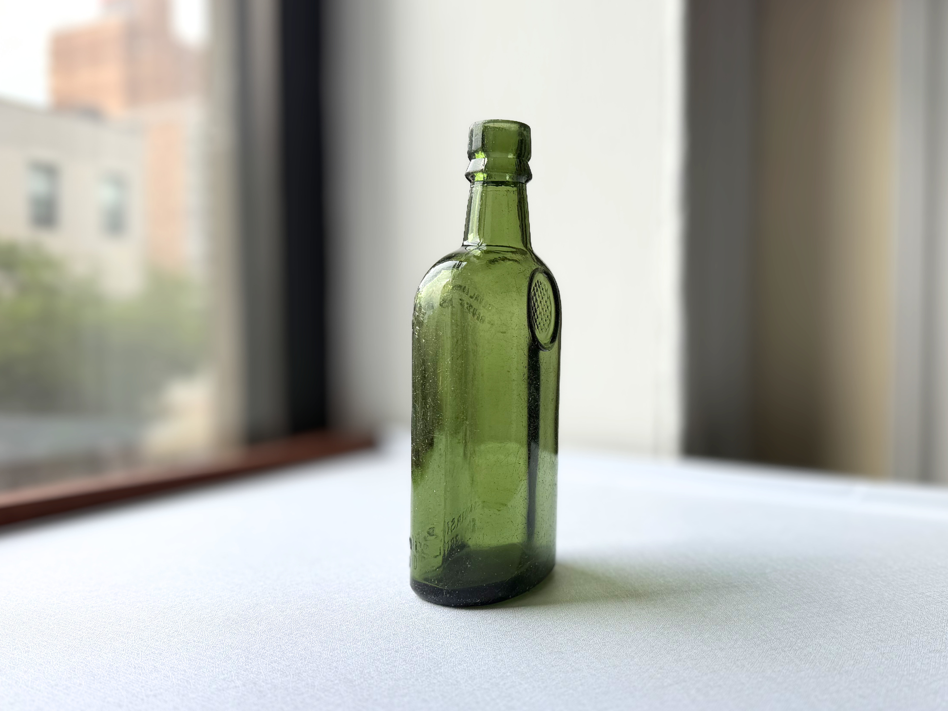 Vintage deep green glass bottle embossed William Sanderson & Son Ltd. Leith Scotland, shown at a three-quarter angle highlighting its rounded silhouette and subtle surface haze from decades along NYC's shoreline. A striking bar cart or Neo Deco shelf accent.
