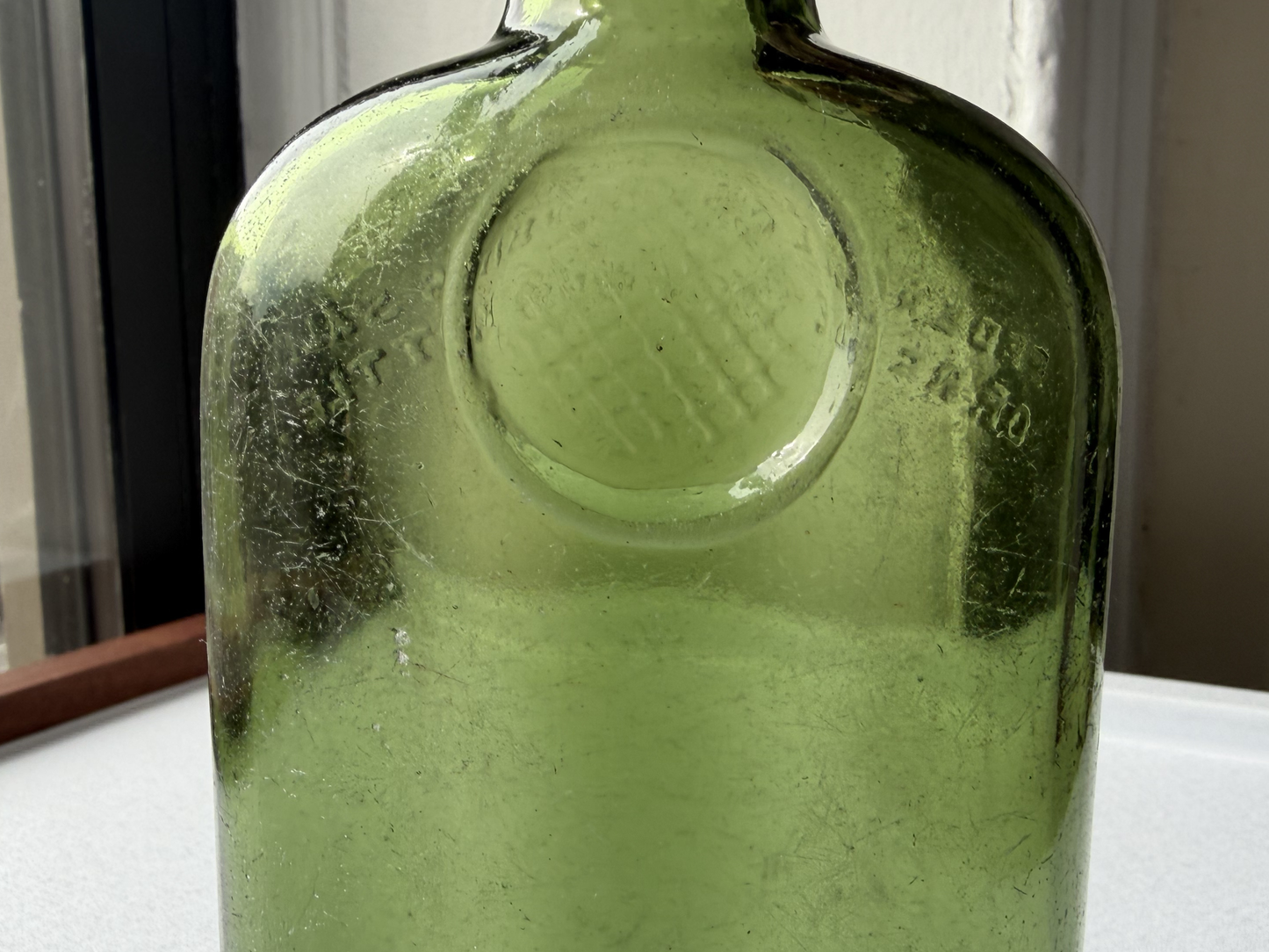 Close-up of the round embossed emblem design on the back of a vintage green glass William Sanderson & Son bottle, showing crisp detail preserved despite decades of age.