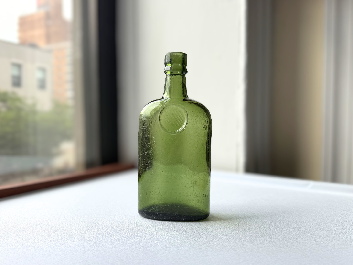Full length view of a vintage green glass Sanderson bottle standing upright, showcasing its rounded body, tapered neck, and deep green color against a neutral background.
