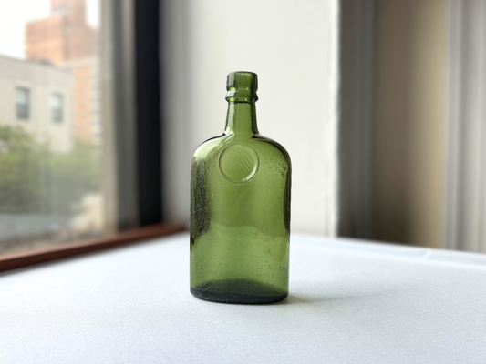 Full length view of a vintage green glass Sanderson bottle standing upright, showcasing its rounded body, tapered neck, and deep green color against a neutral background.