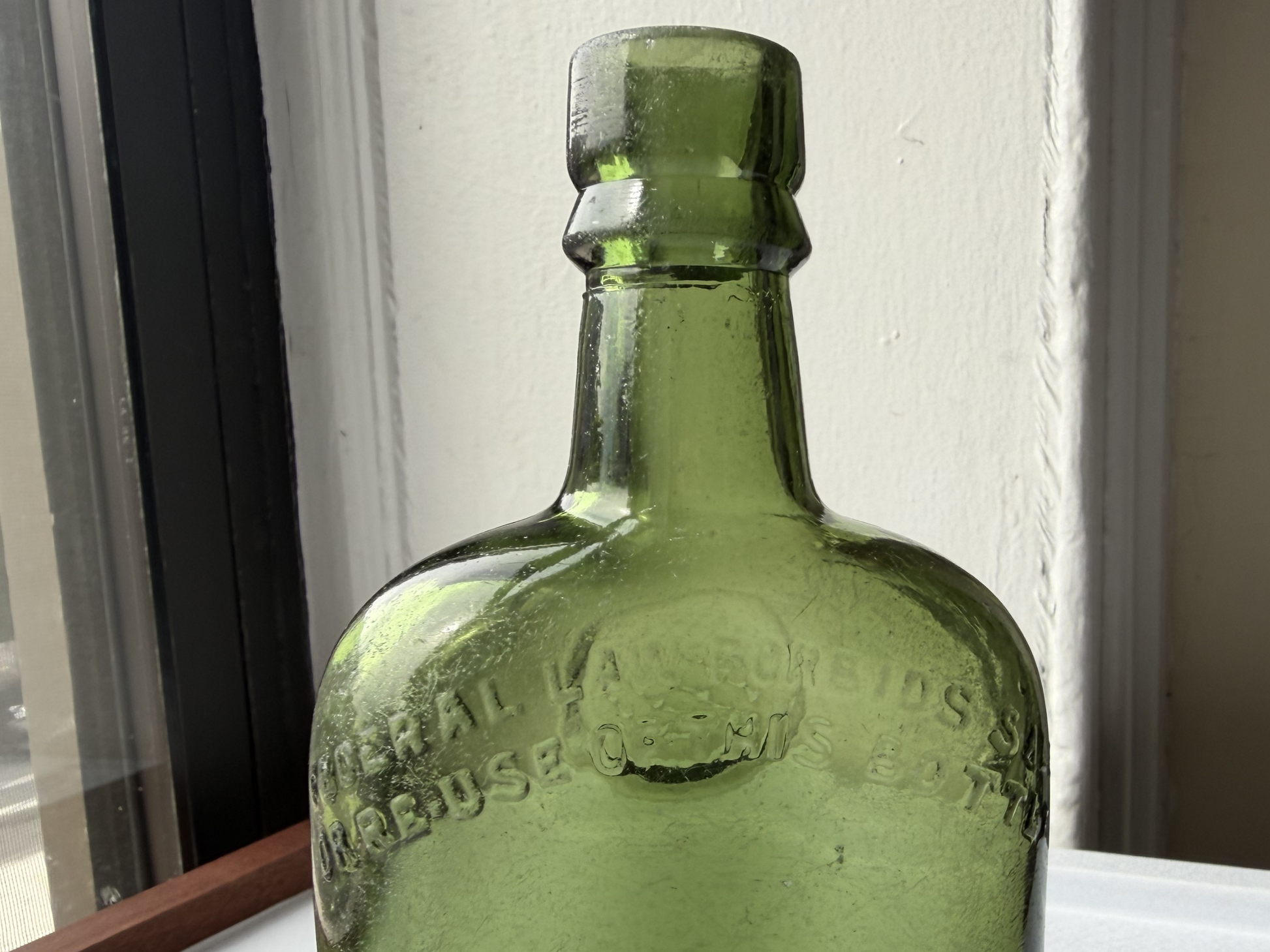Close-up of the shoulder area of a vintage green glass Sanderson bottle, showing the faint natural haze and minor surface scratches consistent with decades spent along NYC's historic shoreline.